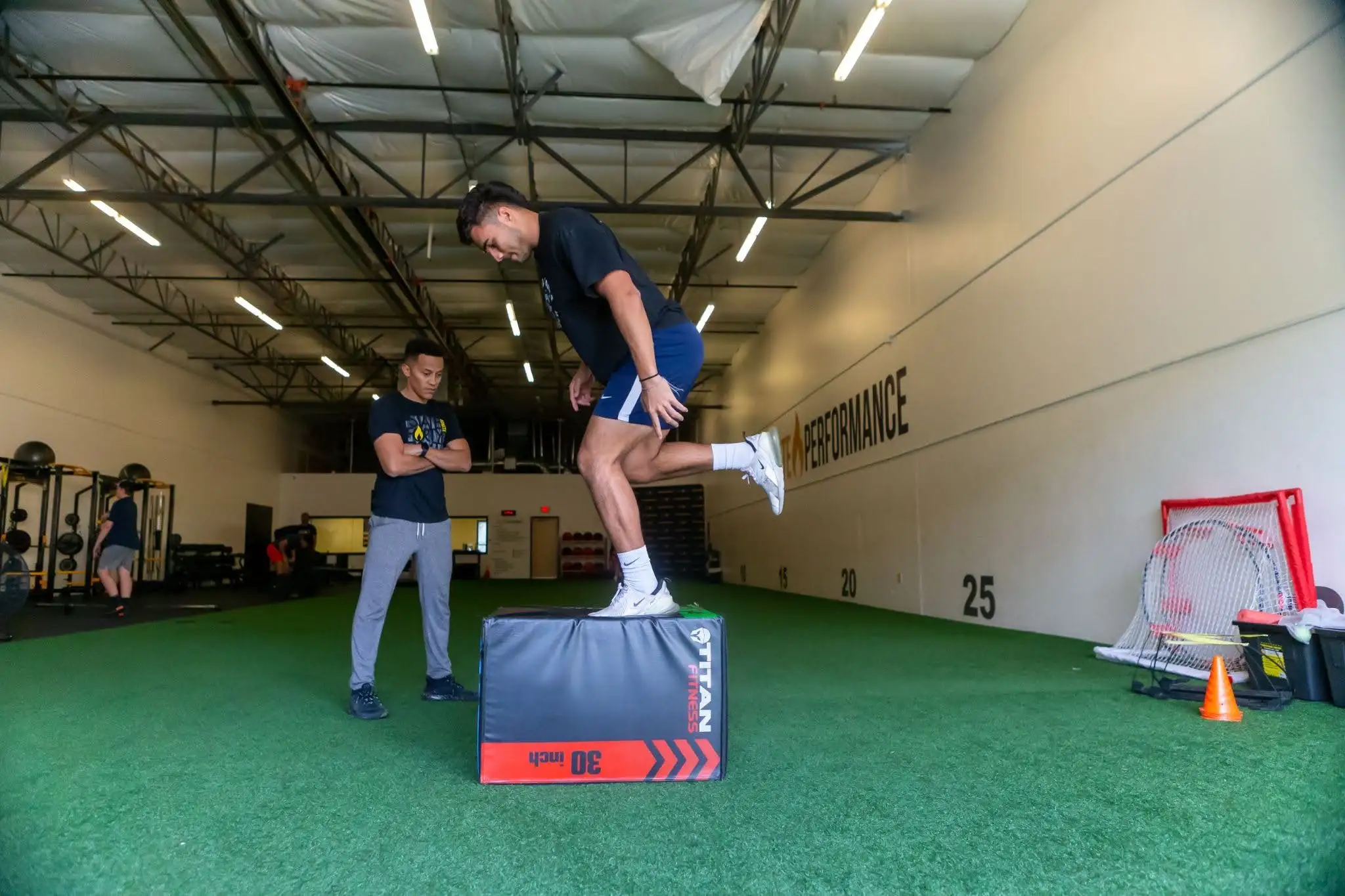 Athlete performing a plyometric box jump with coach supervision in a gym