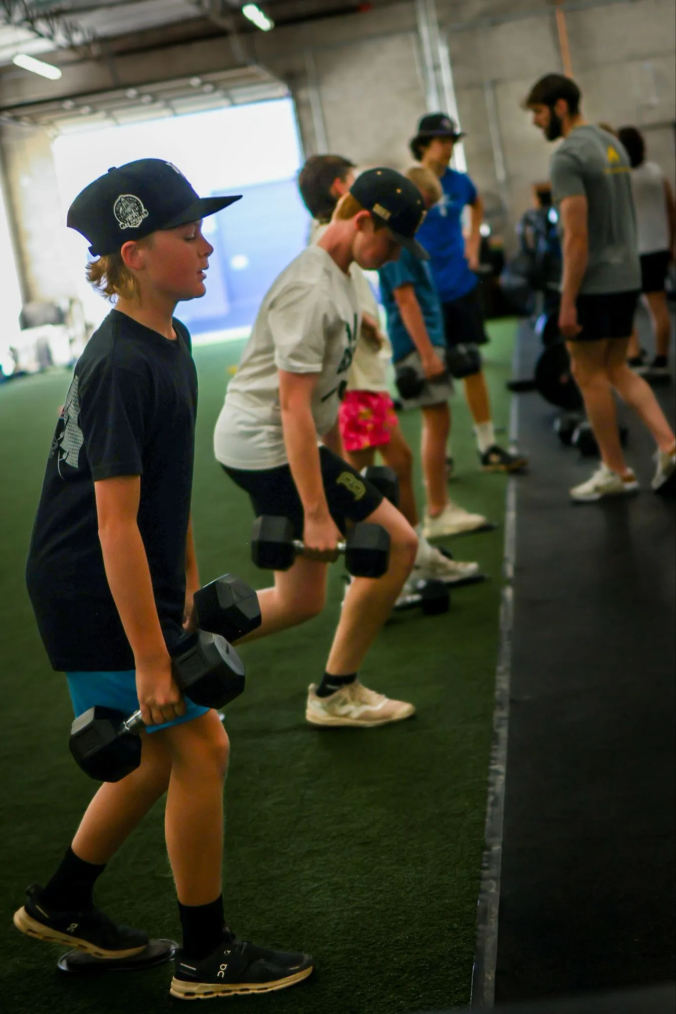 Young athletes performing dumbbell split squats on turf during a group strength training session at Ignite Performance